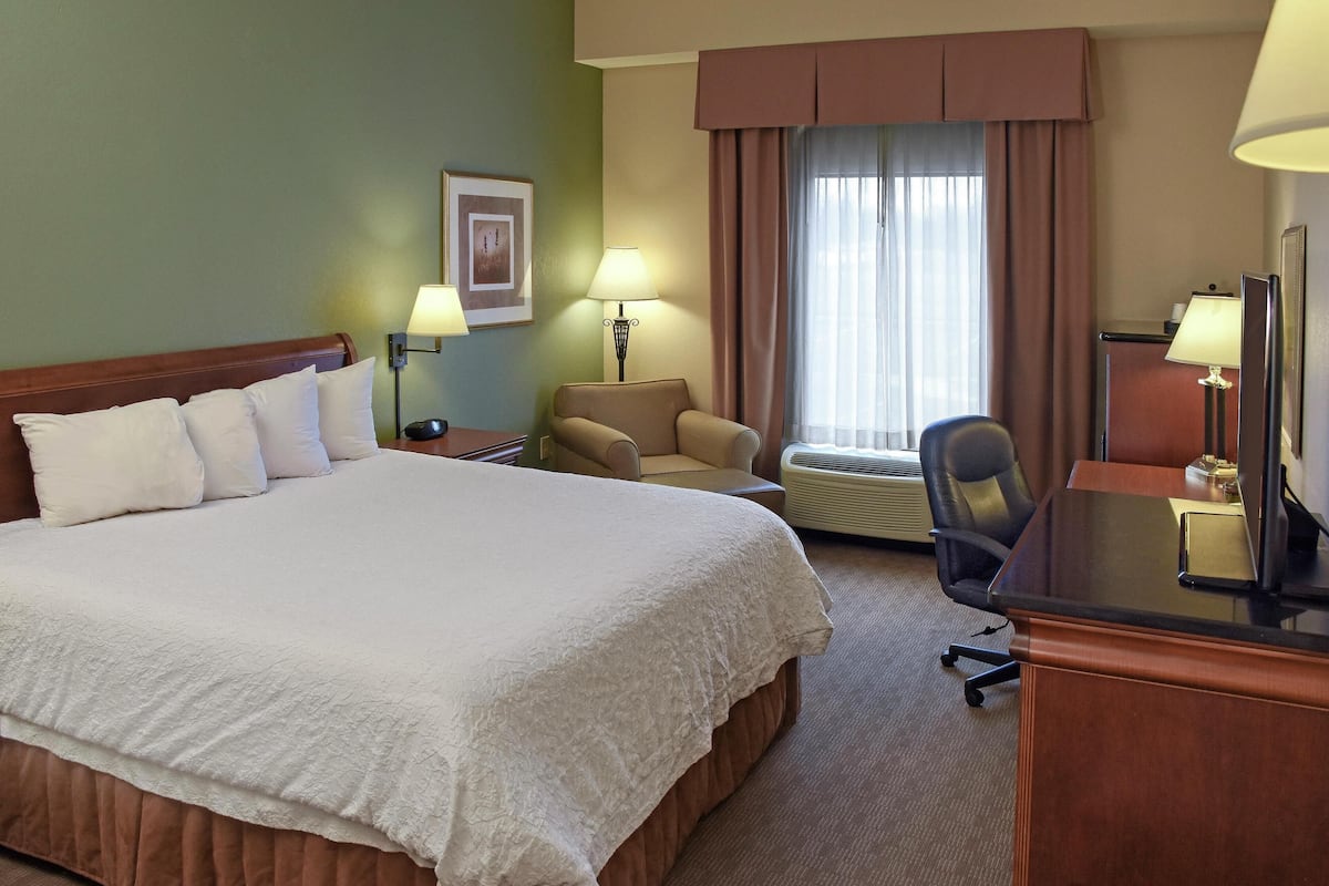 A hotel room with a large bed, a desk with a computer, a chair, a lamp, and a window with curtains.