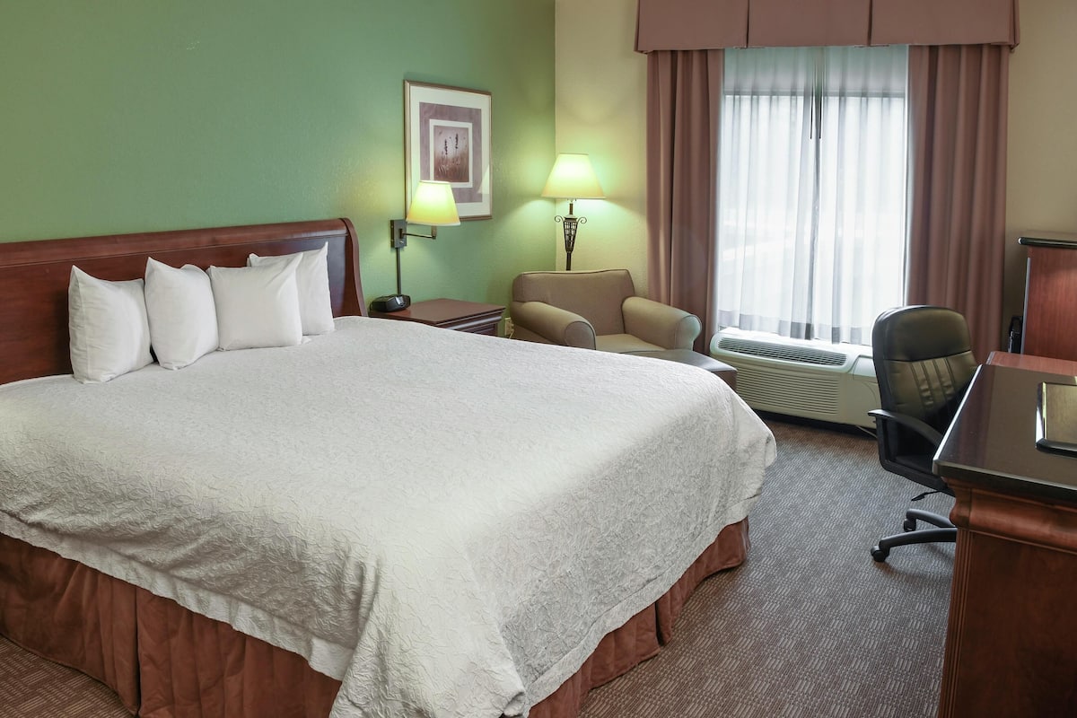 A hotel room with a large bed, two bedside lamps, a chair, a desk, and a window with curtains.