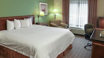 A hotel room with a large bed, two bedside lamps, a chair, a desk, and a window with curtains.