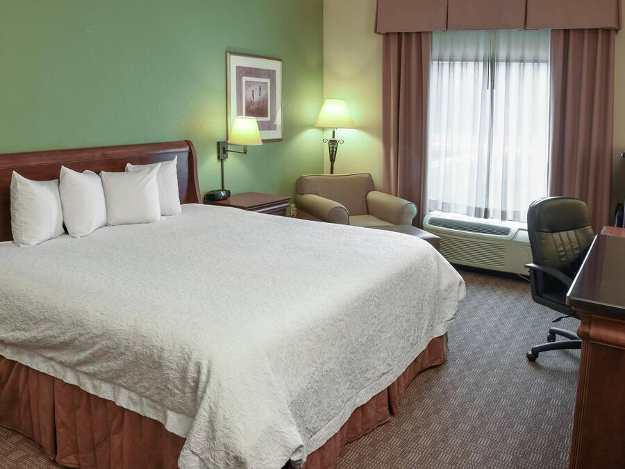 A hotel room with a large bed, two bedside lamps, a chair, a desk, and a window with curtains.