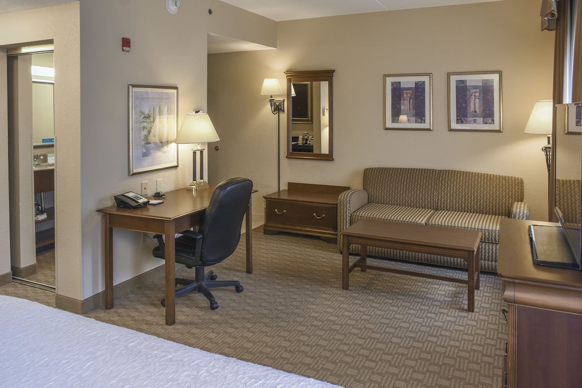 A hotel room with a bed, a desk with a chair, a sofa, a small table, and a dresser.