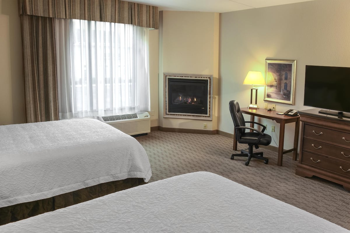 A hotel room with two beds, a desk, a chair, a television, a fireplace, and a lamp.