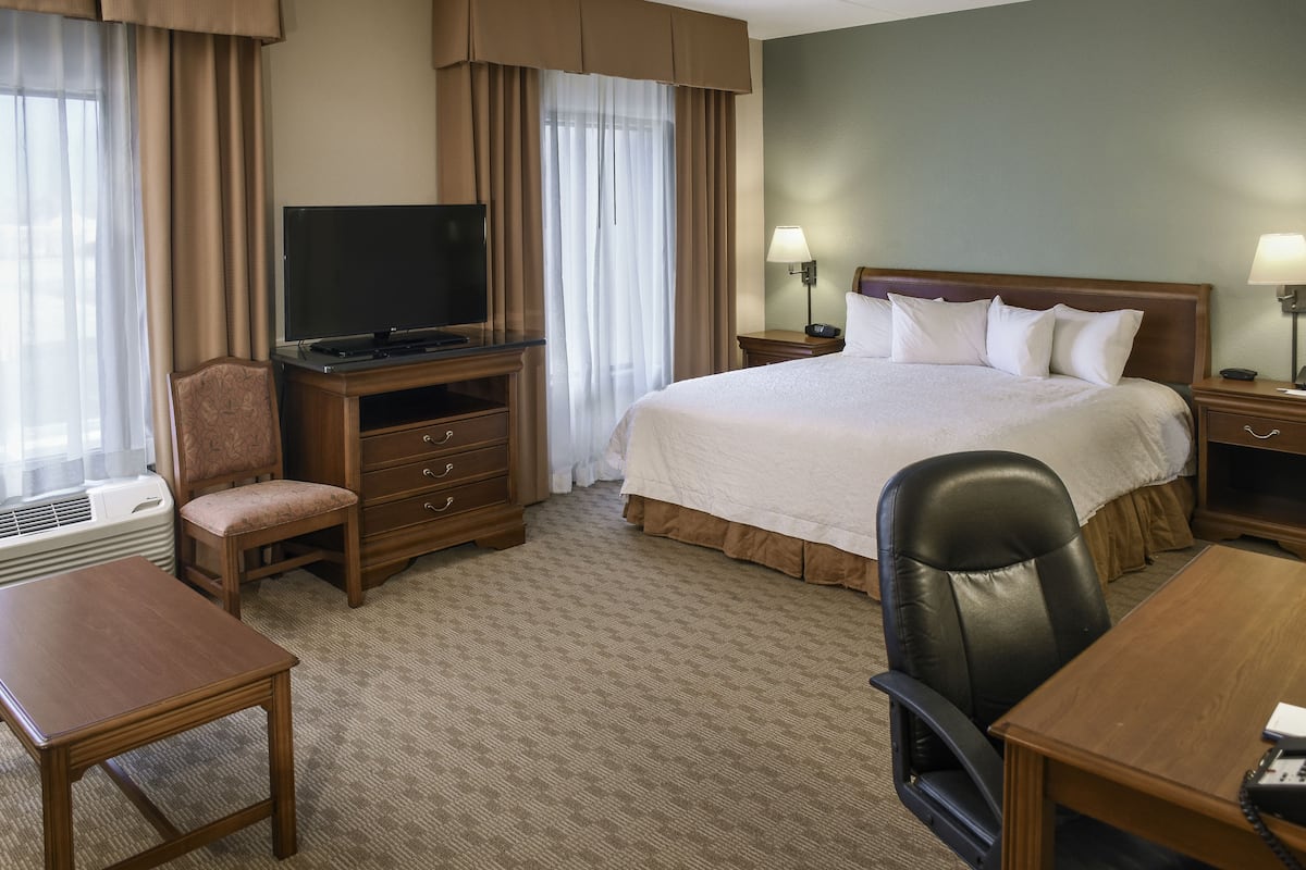 A hotel room with a bed, a desk, a chair, a television, and two bedside lamps.