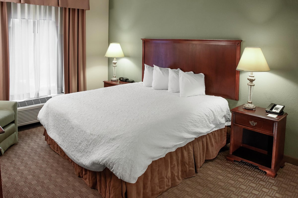 A hotel room with a large bed, two bedside tables with lamps, a chair, and a window with curtains.