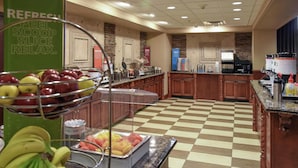 Un'area buffet con frutta, distributori di bevande, pavimento a scacchi e una macchina per il caffè.