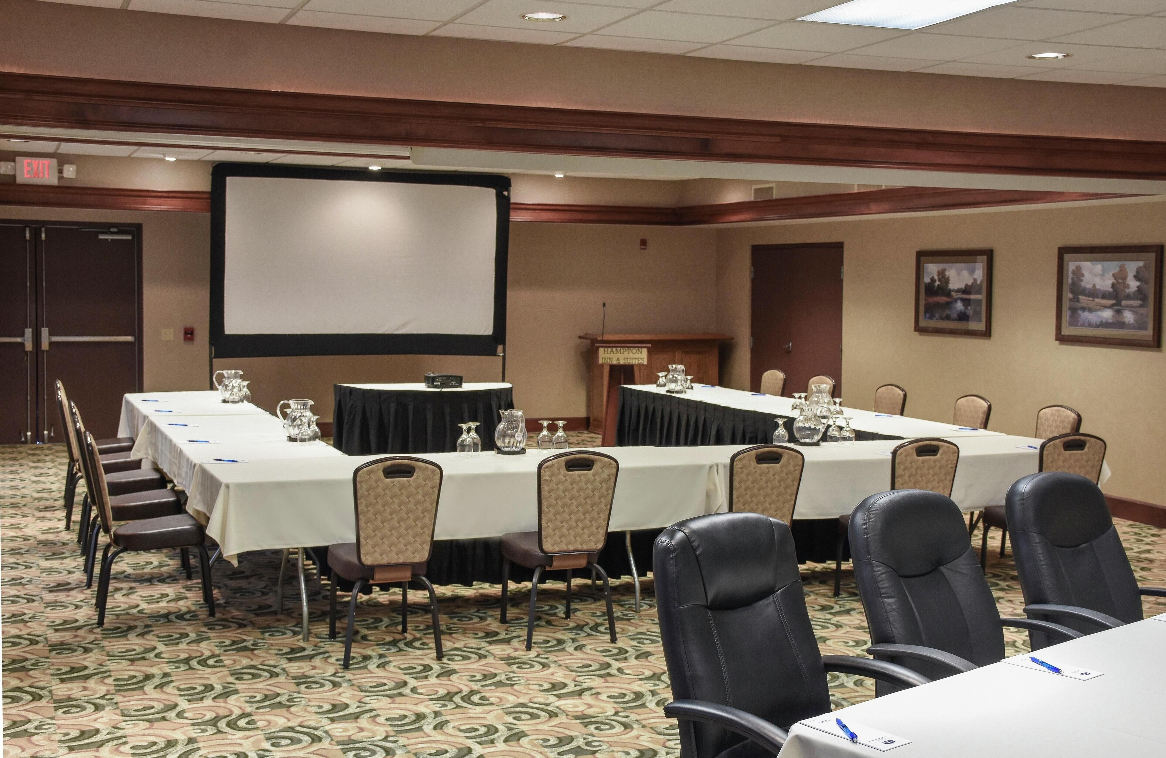 A conference room with a long table, chairs, a projector screen, and a podium.