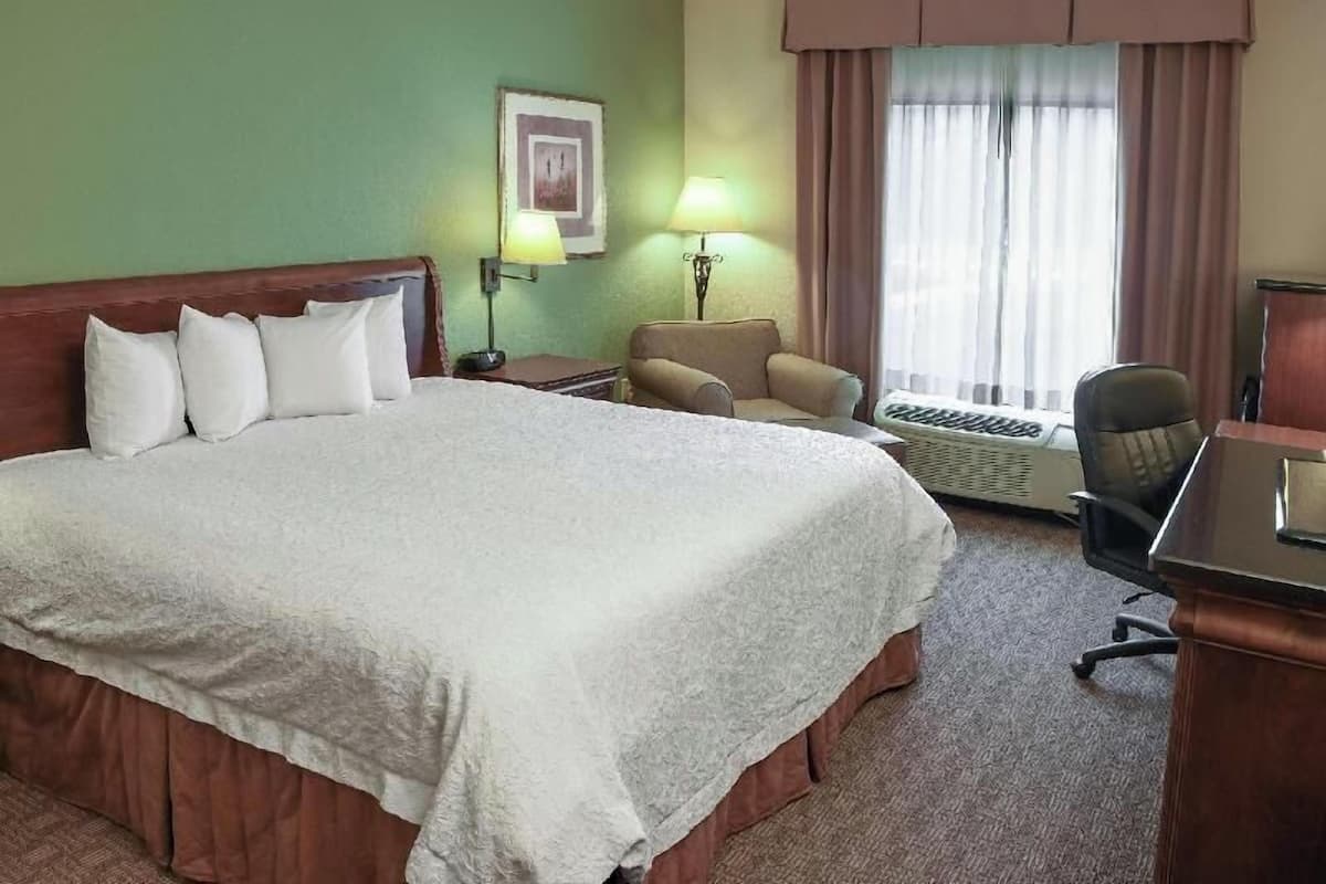 A hotel room with a large bed, a desk, a chair, a lamp, and a window with curtains.