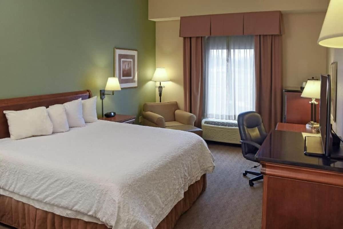 A hotel room with a large bed, a desk, a chair, a lamp, and a window with curtains.