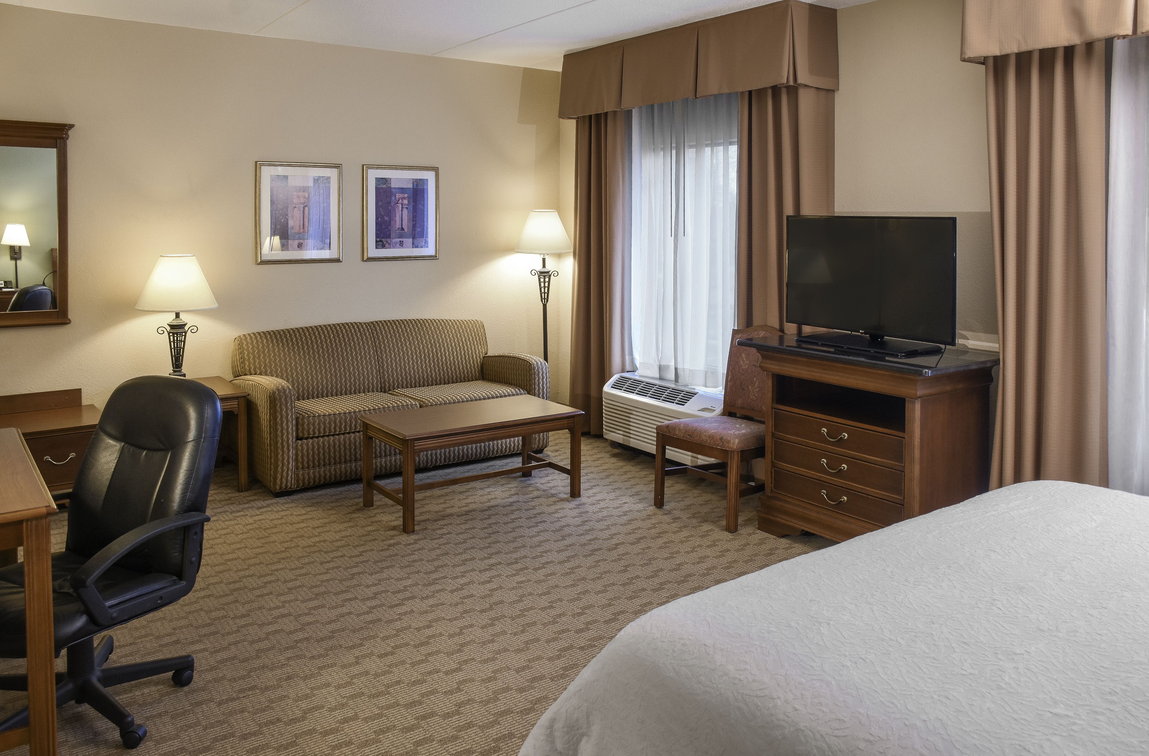 Ein Hotelzimmer mit einem Bett, einem Schreibtisch mit Stuhl, einer Couch, einem Fernseher und zwei Lampen.