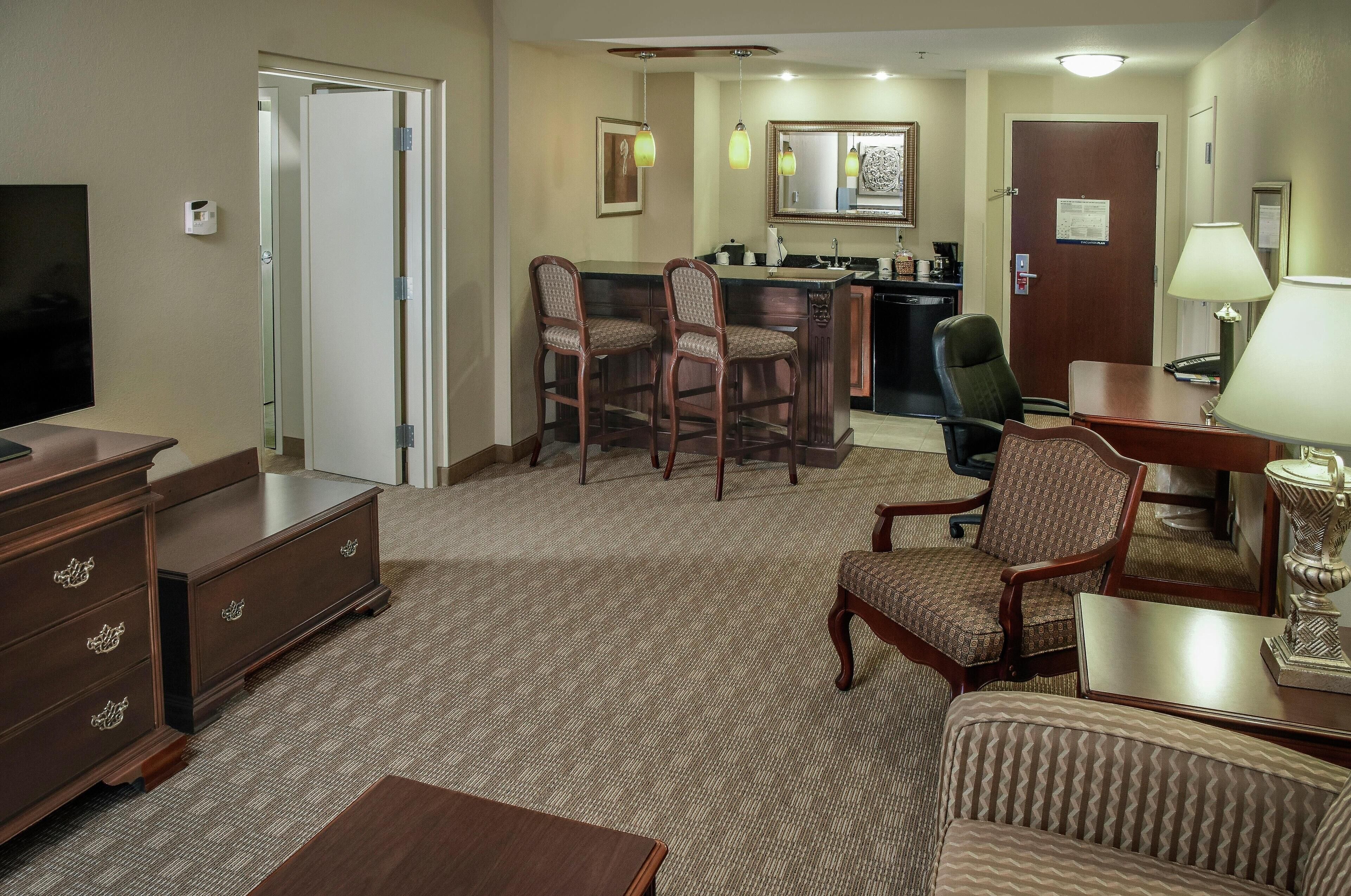 A hotel room with a TV, a desk, a chair, a sofa, and a small dining area with chairs and a table.