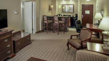 A hotel room with a TV, a desk, a chair, a sofa, and a small dining area with chairs and a table.