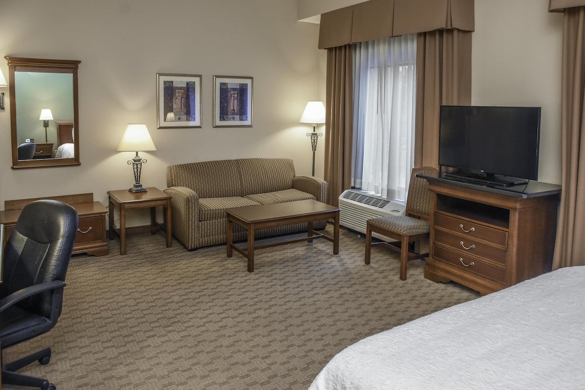 A hotel room with a bed, a desk, a chair, a sofa, a television, a lamp, and two framed pictures on the wall.