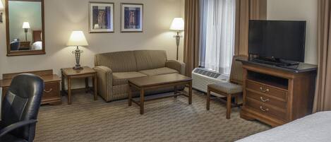 A hotel room with a bed, a desk, a chair, a sofa, a television, a lamp, and two framed pictures on the wall.