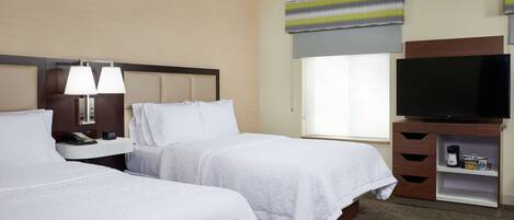 A hotel room with two beds, a TV, a bedside table with a lamp, and a window with a view.