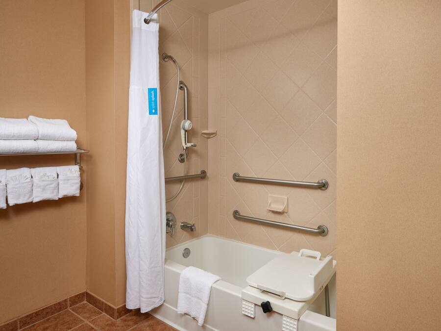 Ein Badezimmer mit einer Badewanne, einer Dusche inklusive Haltegriff und einem Ablagebereich mit gefalteten Handtüchern.