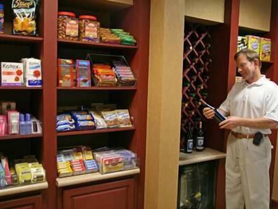 Un hombre con bata blanca parado en una despensa llena de diversos alimentos y productos.