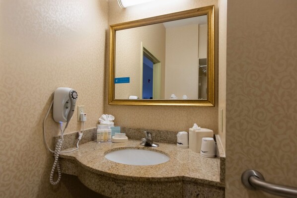 A bathroom with a granite sink, a mirror, a hairdryer, and toiletries.