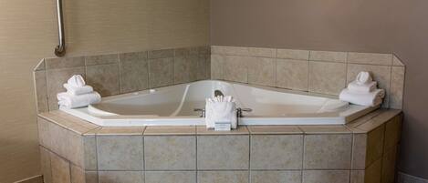 A corner bathtub with a grab bar, towels, and a handheld showerhead.