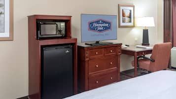 A hotel room with a bed, a desk with a computer, a refrigerator, a microwave, a lamp, and a Hampton Inn sign.