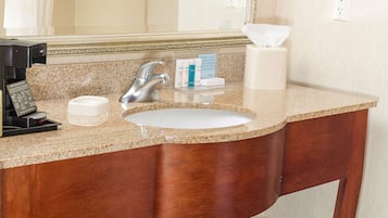 Un bany amb taulell de granit, un lavabo, una cafetera i productes de tocador.