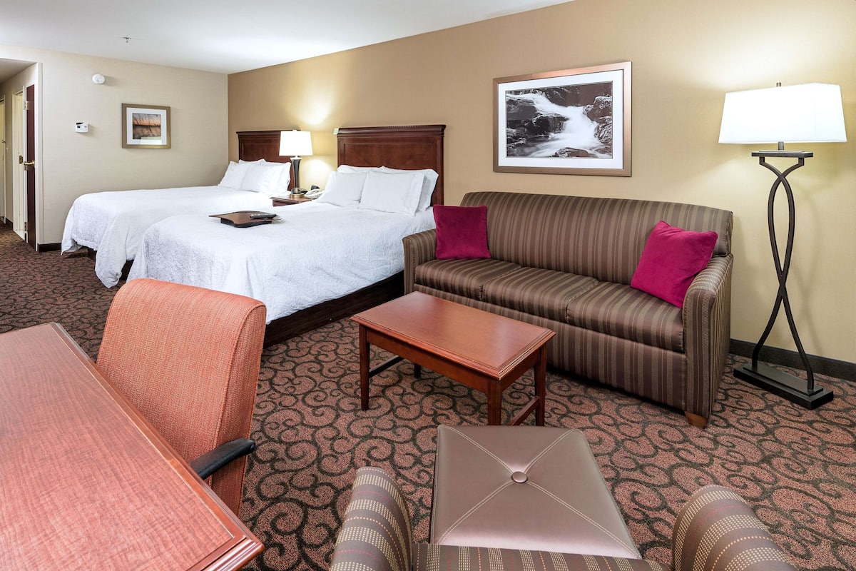 A hotel room with two beds, a sofa, a table, and a chair.