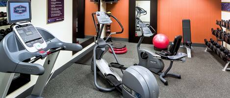 A gym with treadmills, an elliptical, a stationary bike, a red exercise ball, and a wall-mounted TV.