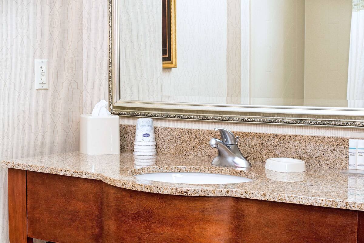 A bathroom with a granite countertop, a sink, a mirror with a gold frame, and a towel dispenser.