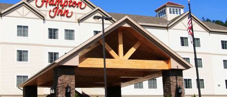A Hampton Inn hotel with a prominent entrance, a covered parking area, and a landscaped flower bed in front.