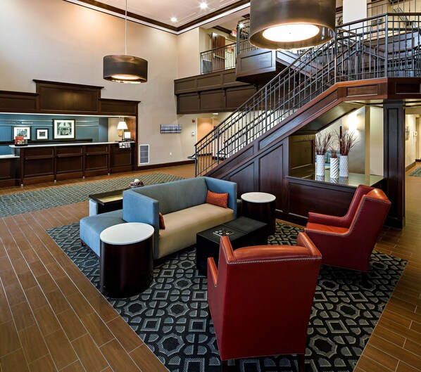 A lobby with a reception desk, seating area with sofas and chairs, a staircase, and a large window.