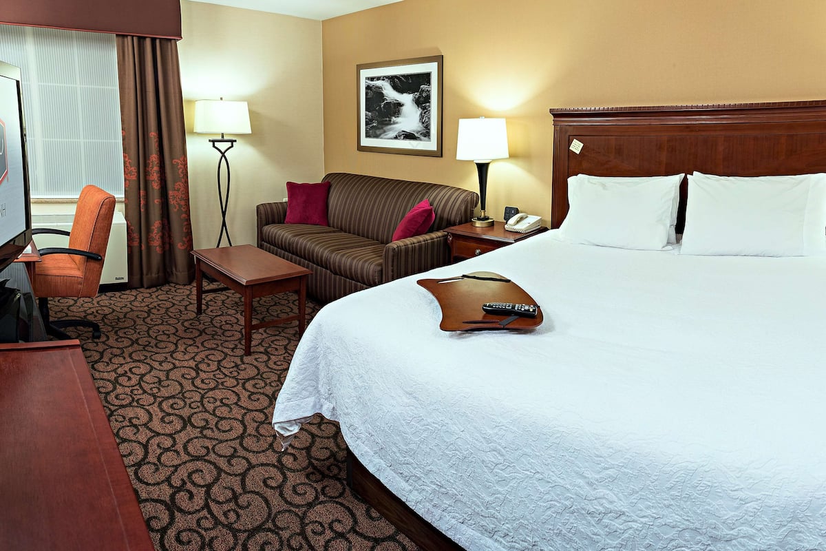 A hotel room with a large bed, a desk, a chair, a sofa, and a lamp.