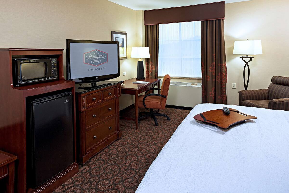 A hotel room with a bed, a desk, a chair, a television, a microwave, and a lamp.