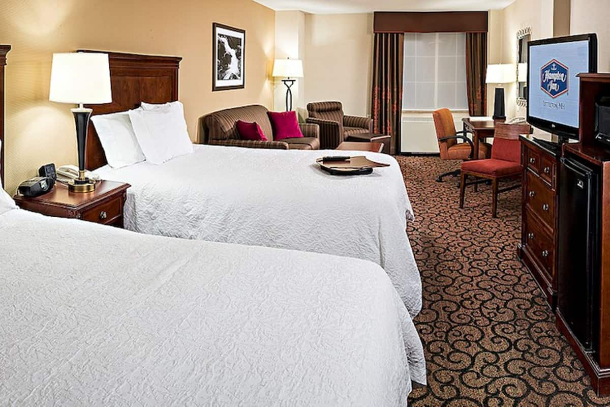 A hotel room with two beds, a desk, a television, and a dining area.