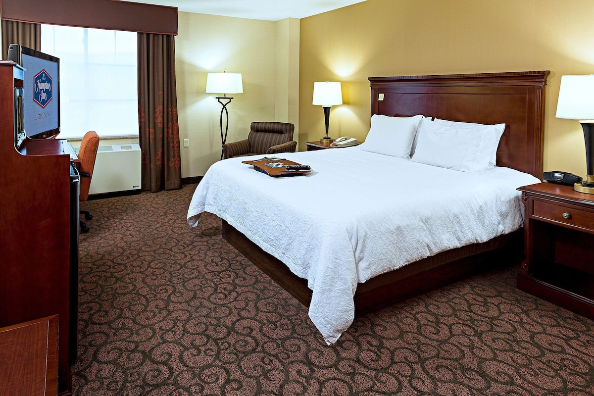 A hotel room with a large bed, two bedside lamps, a desk with a computer, and a view of the outdoors through the window.