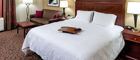 A hotel room with a large bed, a bedside table, a nightstand, a lamp, a telephone, and a couch with a pillow.