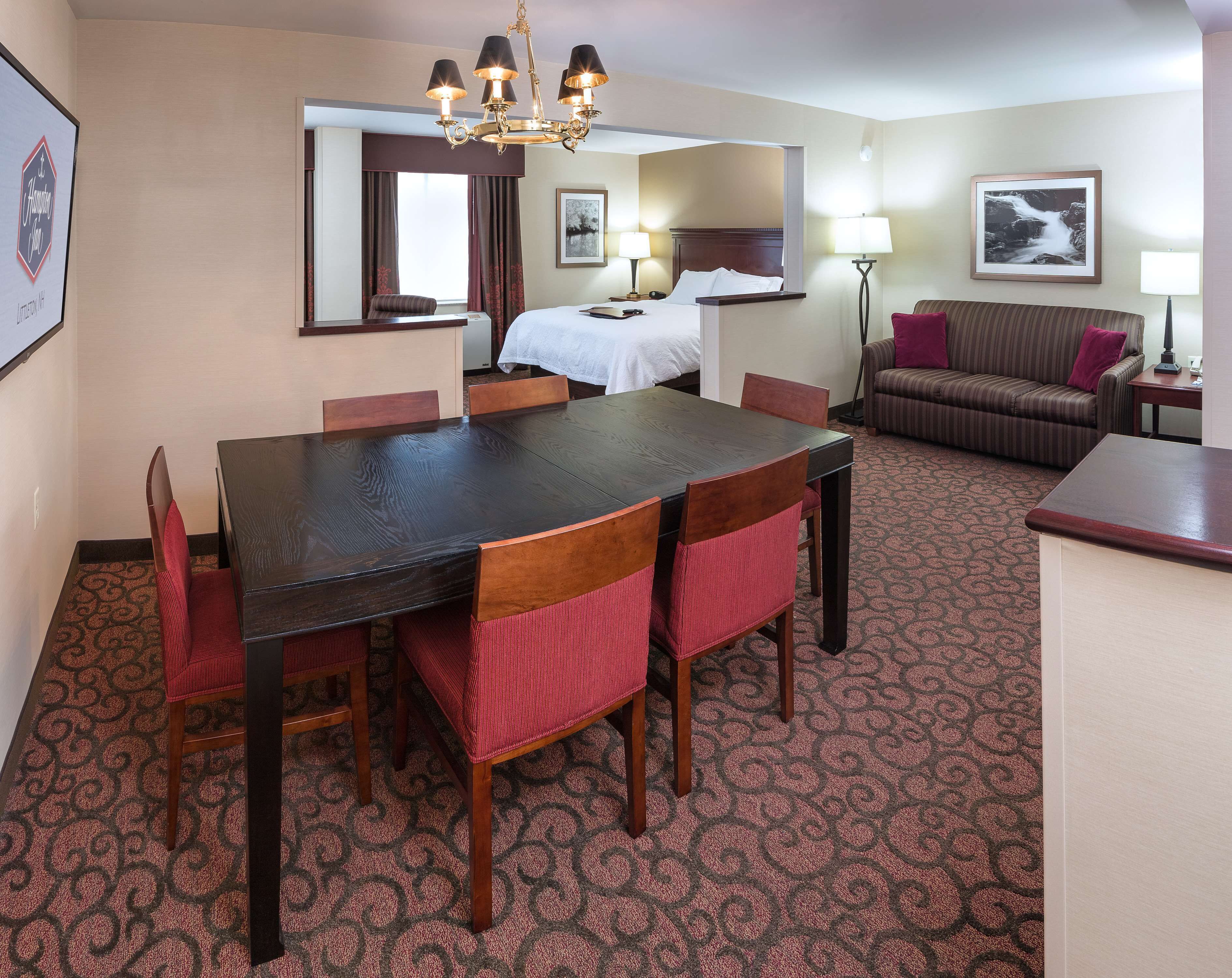 A hotel room with a dining area, a bed, a sofa, and a lamp.