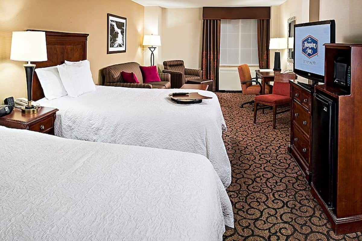 A hotel room with two beds, a desk, a television, and a chair.
