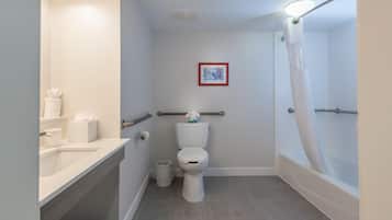 A bathroom with a toilet, a sink, a shower with a curtain, and a framed picture on the wall.