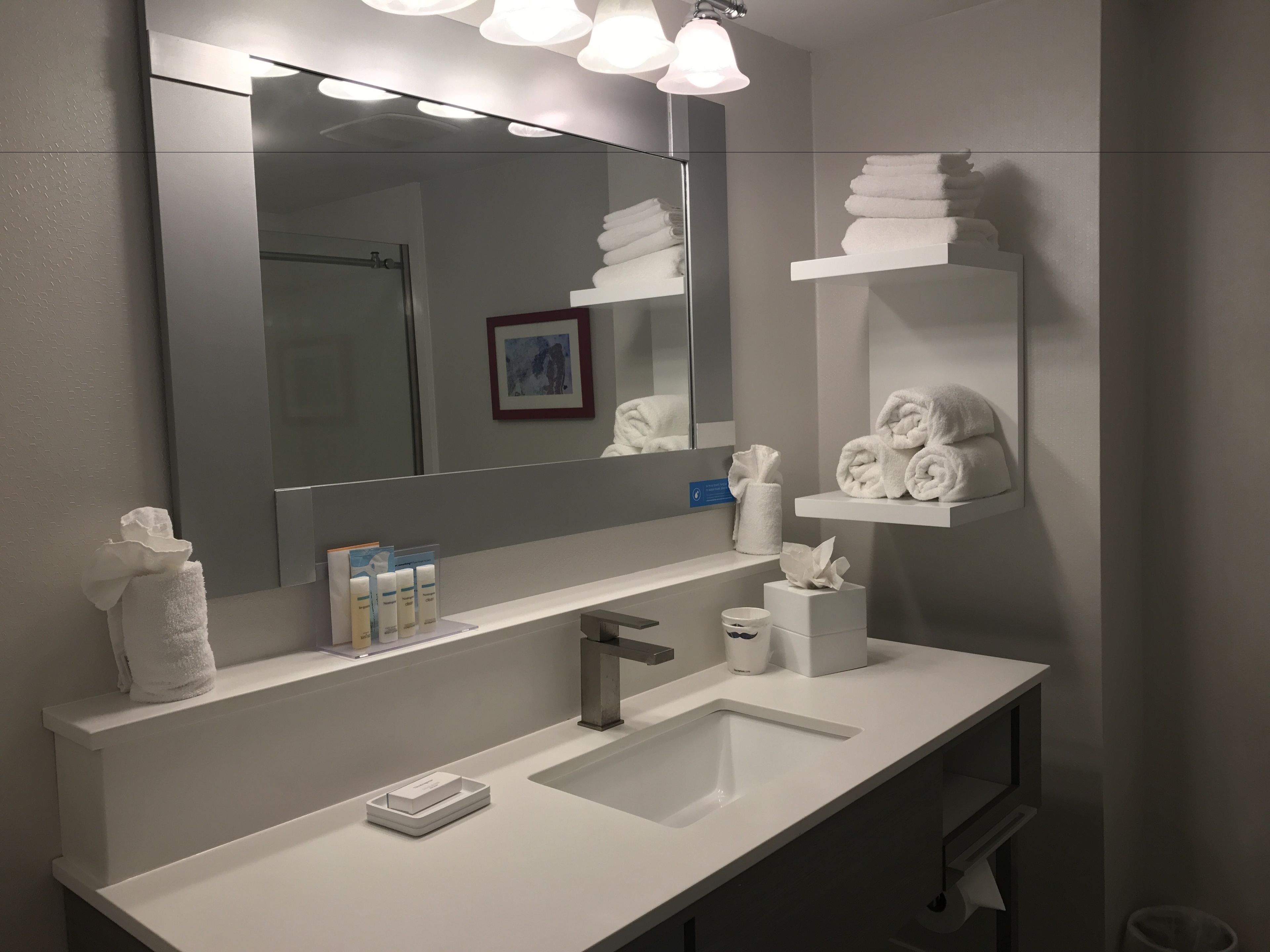 Une salle de bain moderne avec un grand miroir, un lavabo blanc et des porte-serviettes.