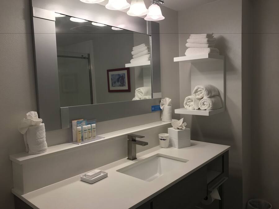 Une salle de bain moderne avec un grand miroir, un lavabo blanc et des porte-serviettes.