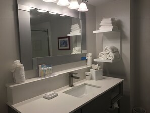 Een moderne badkamer met een grote spiegel, een witte wastafel en handdoekhouders.