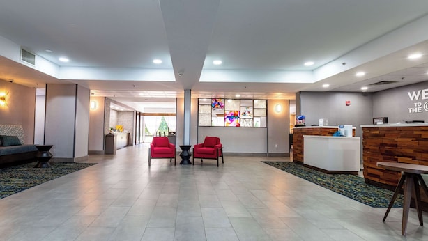 A modern hotel lobby with a reception desk, two red chairs, a sofa, and a kitchen area in the background. - Hampton Inn East Windsor (Hightstown)