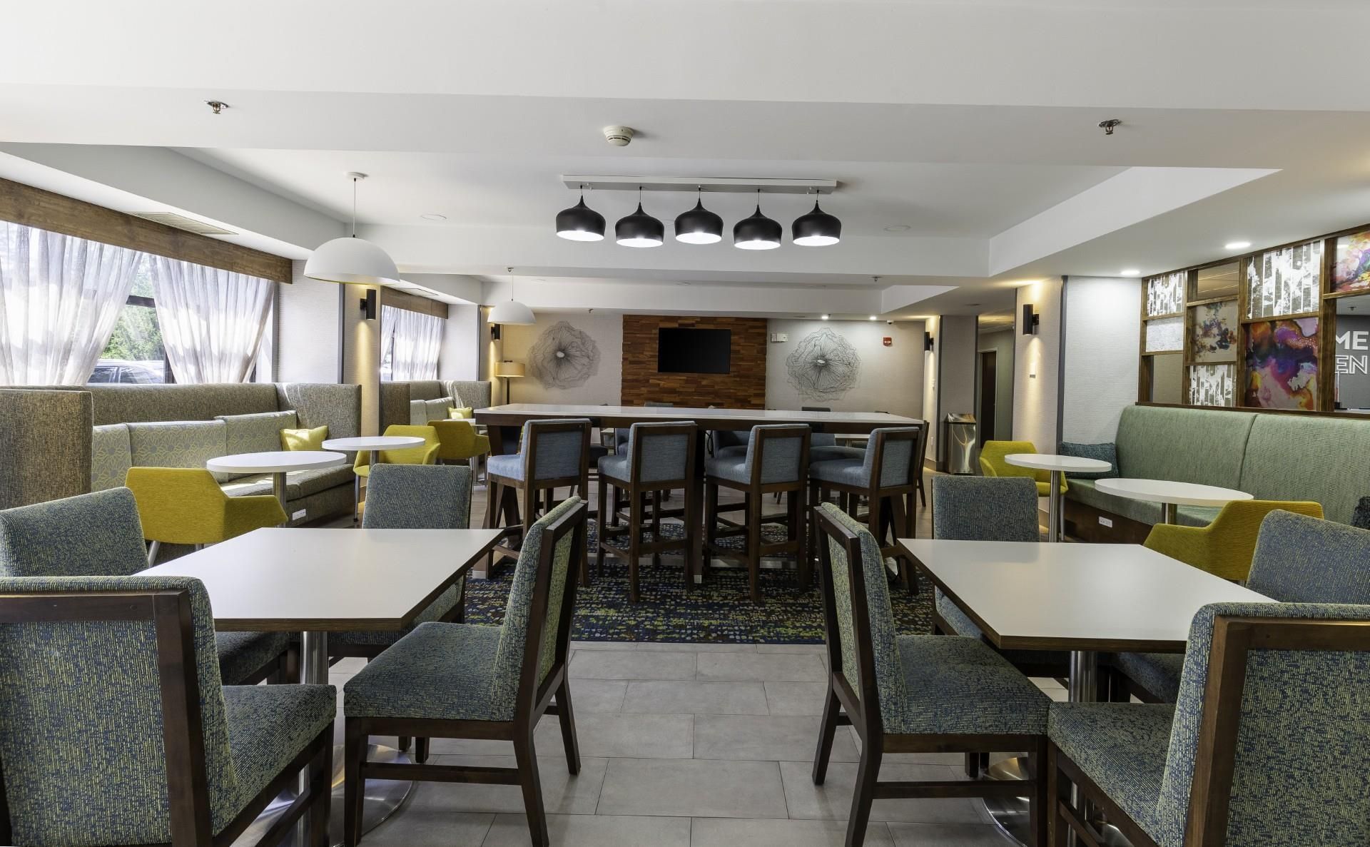 Un comedor de hotel con varias mesas y sillas, una pared central con un panel decorativo y un techo con lámparas colgantes.