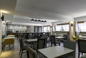 A modern restaurant with multiple seating areas, including tables and booths, and a bar area with a counter. - Hampton Inn East Windsor (Hightstown)