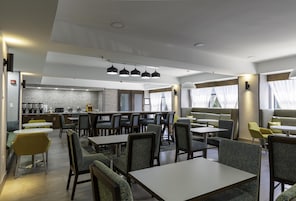 A modern restaurant with multiple seating areas, including tables and booths, and a bar area with a counter.