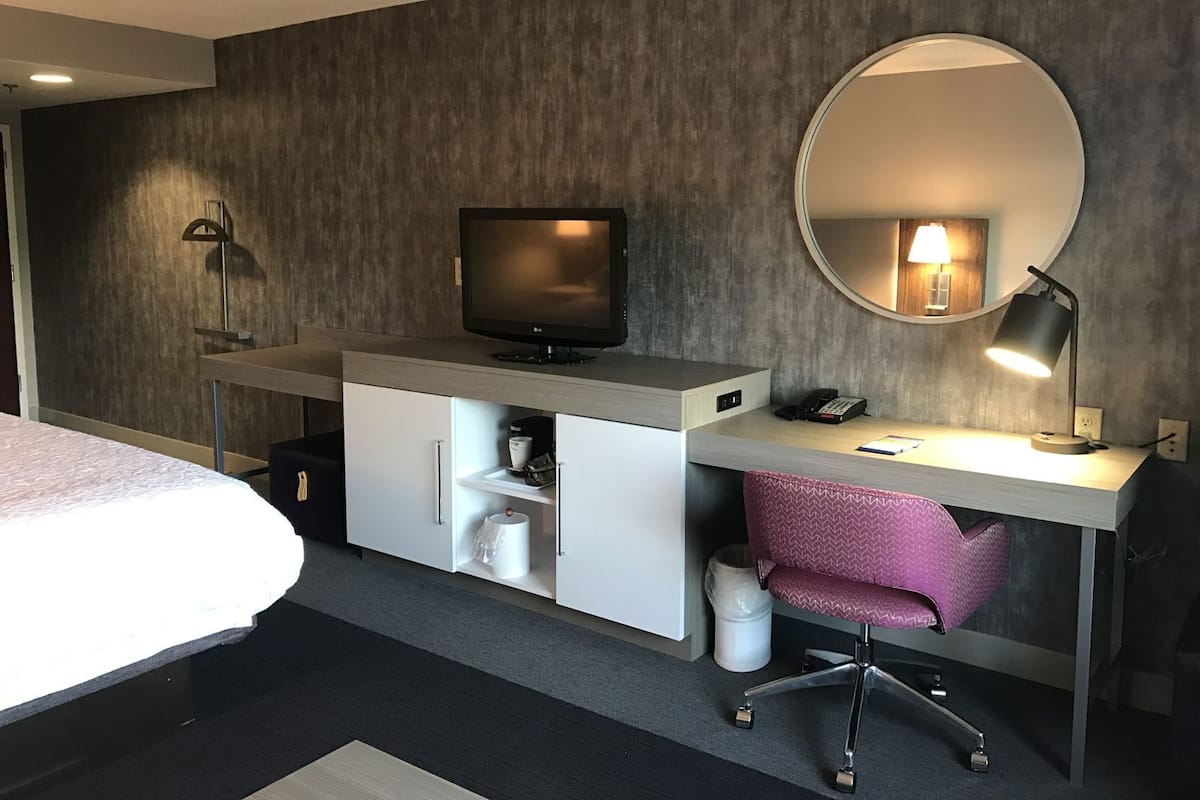 A hotel room with a bed, a desk with a computer, a television, a mirror, and a chair.