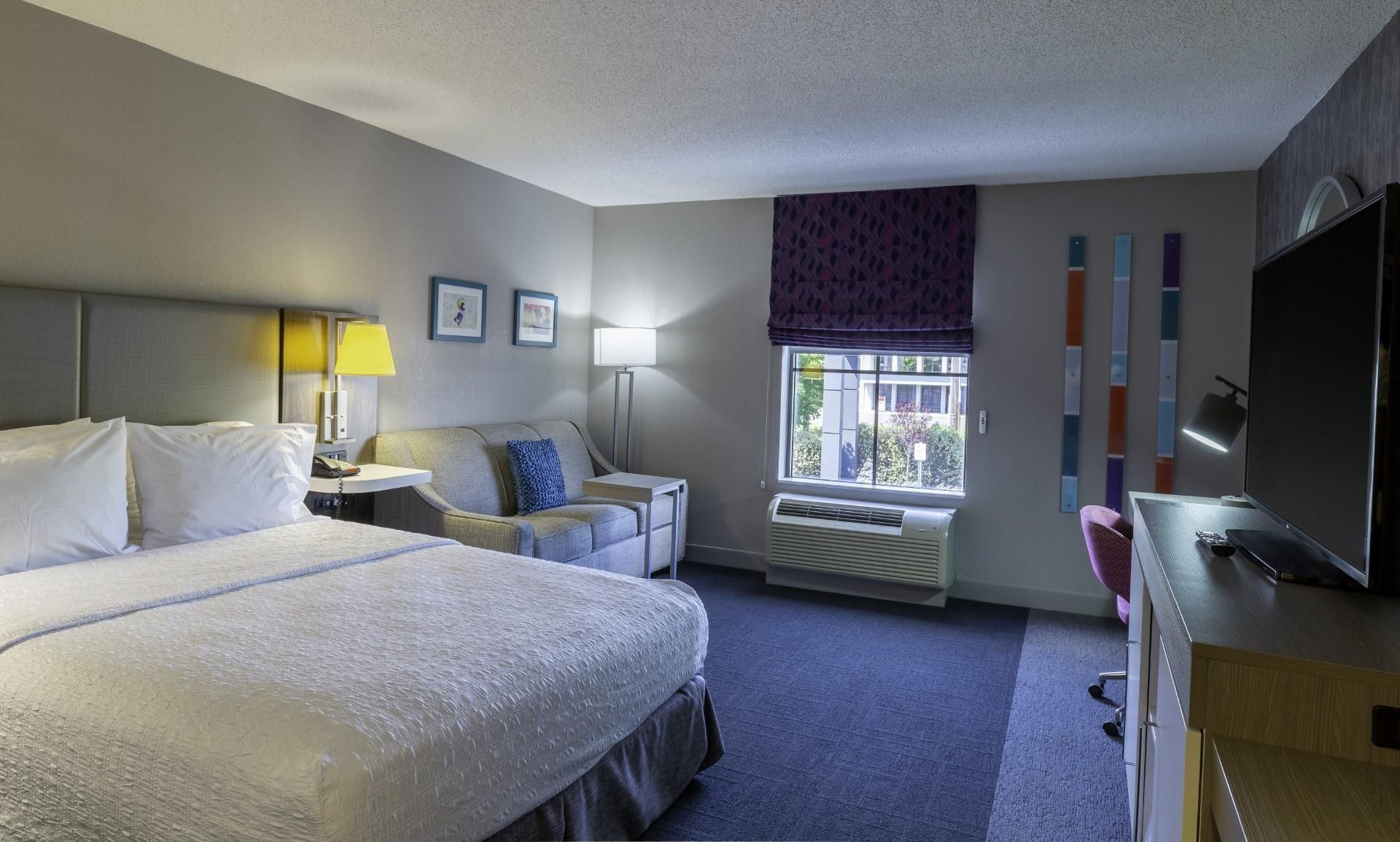 A hotel room with a large bed, a desk, a chair, a window with a view, and a flat-screen TV.