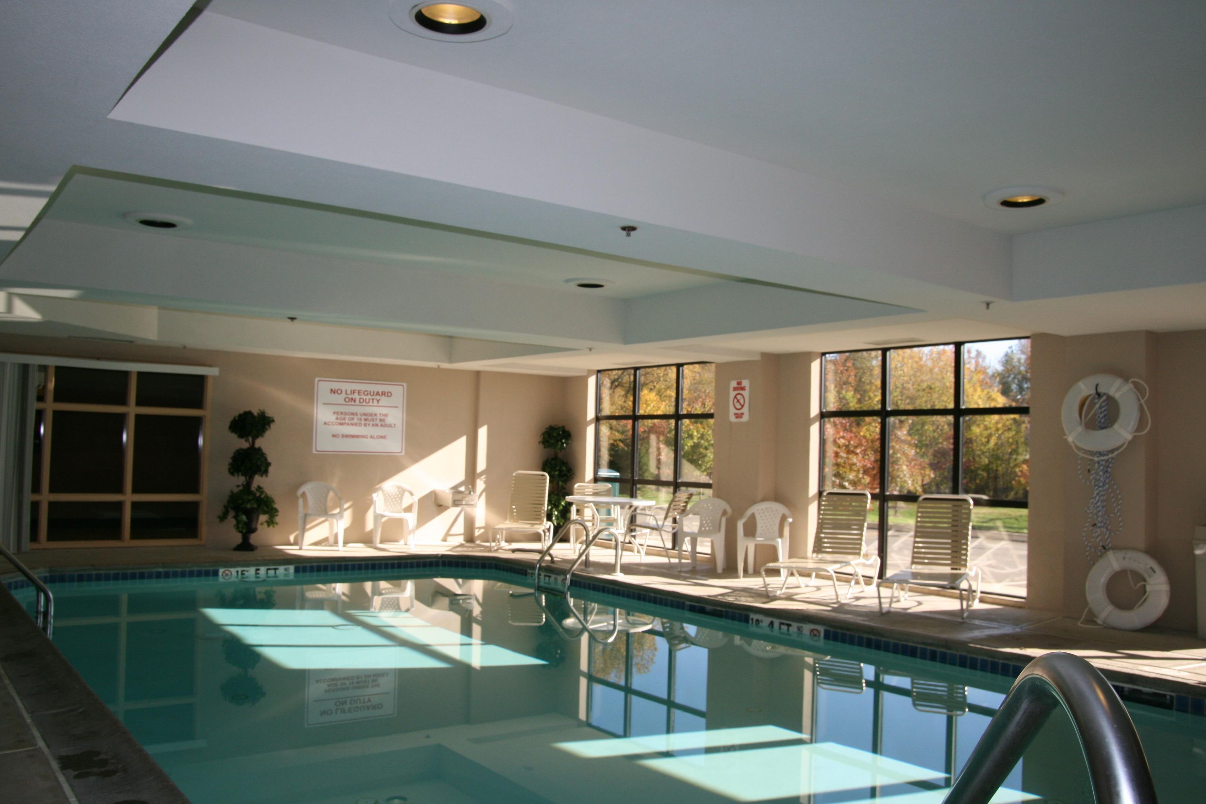 An indoor swimming pool with a lifeguard chair, lounge chairs, and a sign indicating no swimming alone.