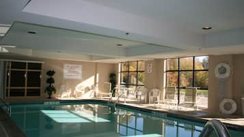 An indoor swimming pool with a lifeguard chair, lounge chairs, and a sign indicating no swimming alone.