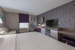 Hotelkamer met een bed, bureau, stoel, televisie en raam met uitzicht op gebouwen.