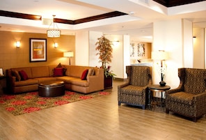 A hotel lobby with a sectional sofa, armchairs, a small table, a potted plant, and a decorative wall.